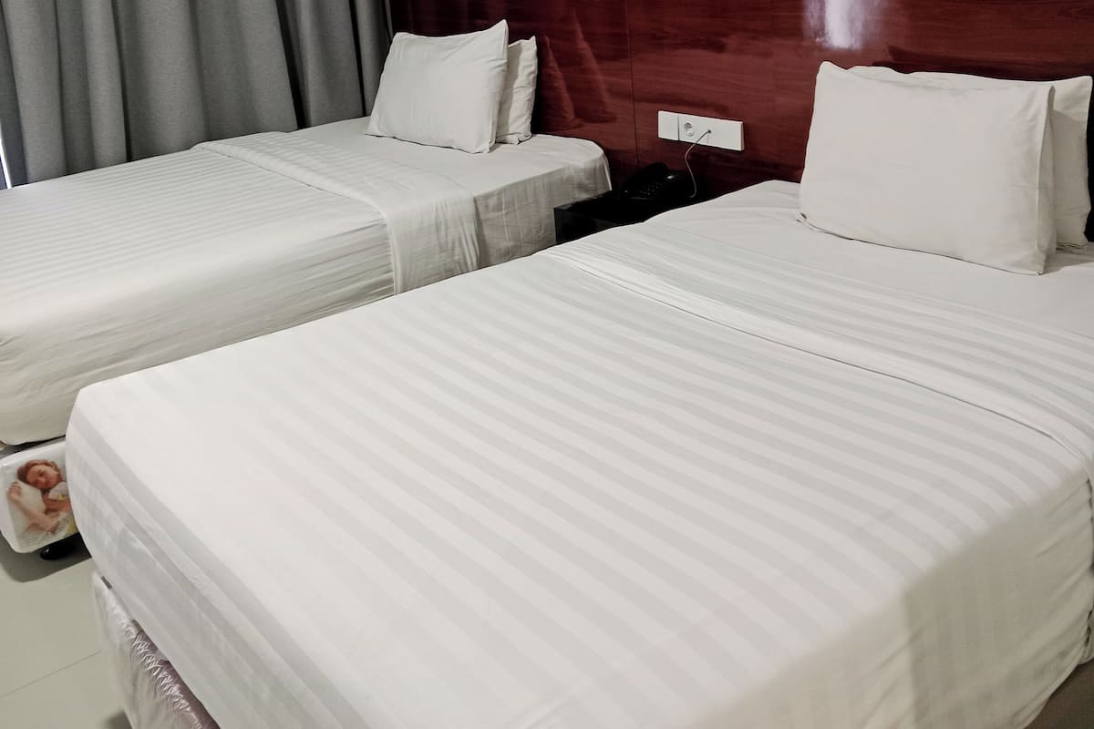 Habitación de hotel con dos camas, cortinas grises, cabecero de madera y una mesita de noche con un teléfono.
