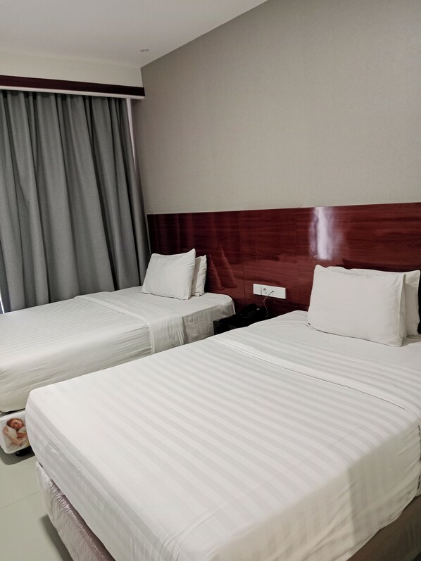 A hotel room with two beds, grey curtains, a wooden headboard, and a bedside table with a phone. - Grand Cahaya Hotel Pangandaran (Pangandaran)