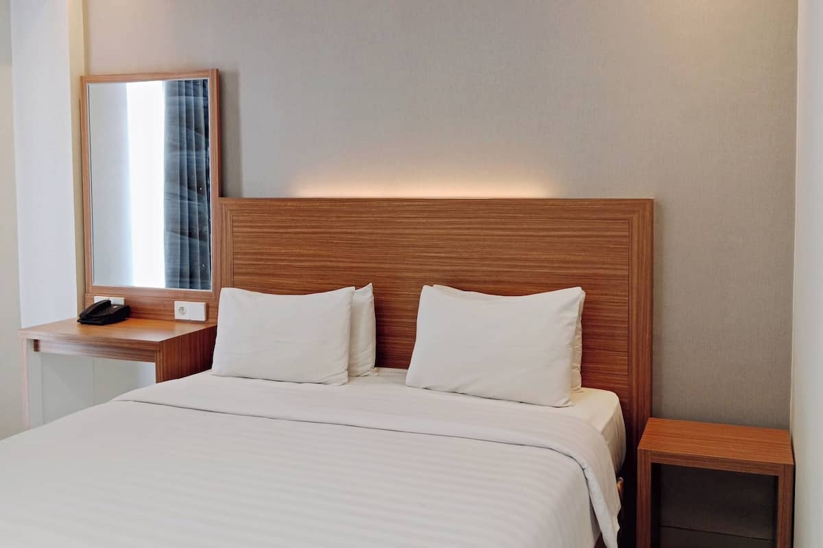 Una habitación de hotel moderna con una cama grande, cabecera de madera, mesitas de noche y un espejo.