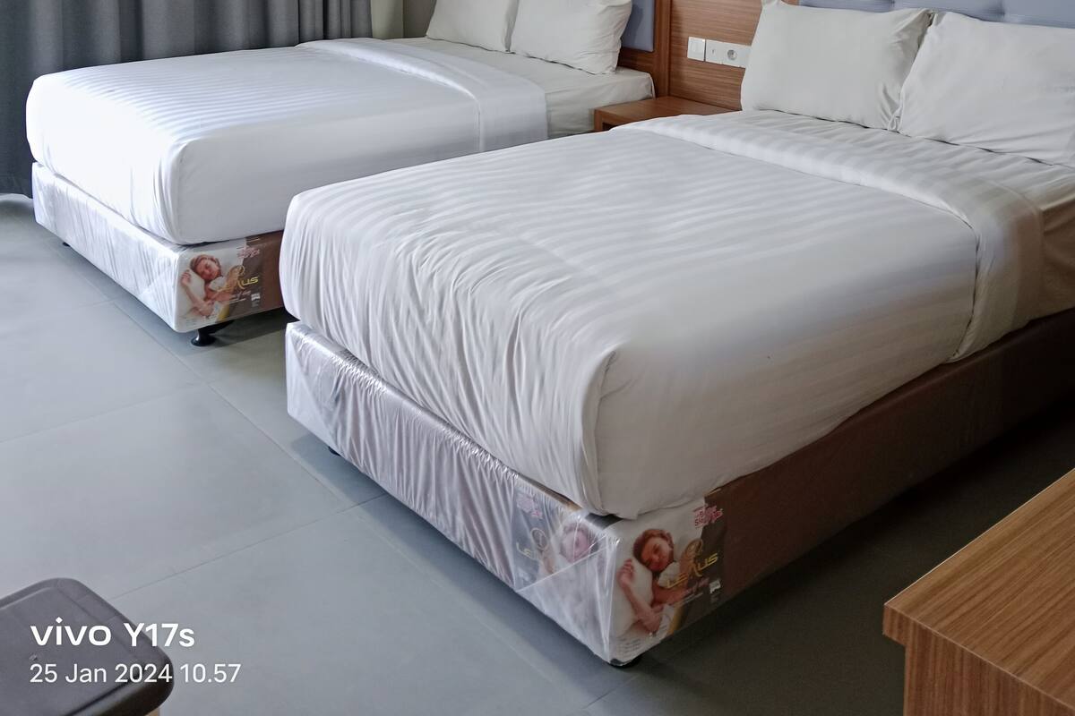 Una habitación de hotel con dos camas, cortinas grises y un cabecero de madera.