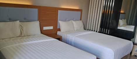 A hotel room with two single beds, wooden headboards, and a large mirror.