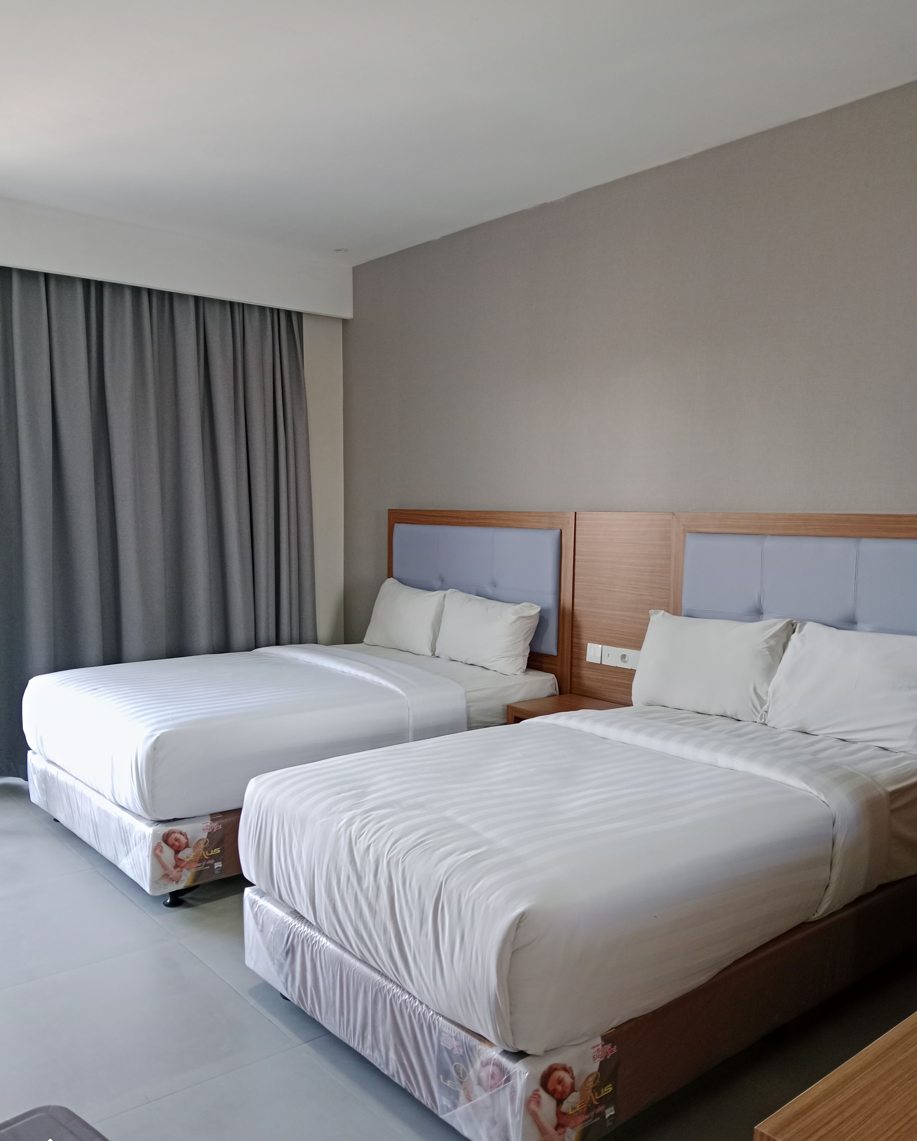 Una habitación de hotel con dos camas, cortinas grises y un cabecero de madera.
