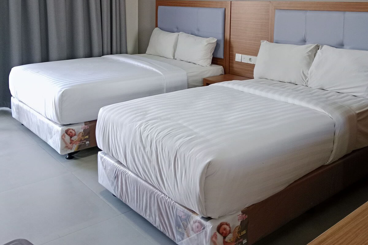 A hotel room with two beds, grey curtains, and a wooden headboard.