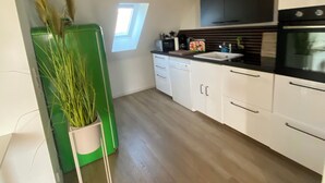Een keuken met houten balken, witte kasten, een groen apparaat en een raam.