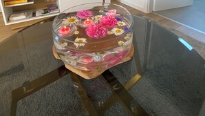 Een woonkamer met een flatscreen-tv, een boekenkast, een schilderij en een decoratieve glazen tafel met bloemen en een kaars.