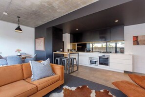 A modern living room with a sofa, a dining table, and a kitchen area with a bar counter. - Stylish light and bright apartment tucked away behind Monument Hill in the Fremantle Art precinct (Fremantle)
