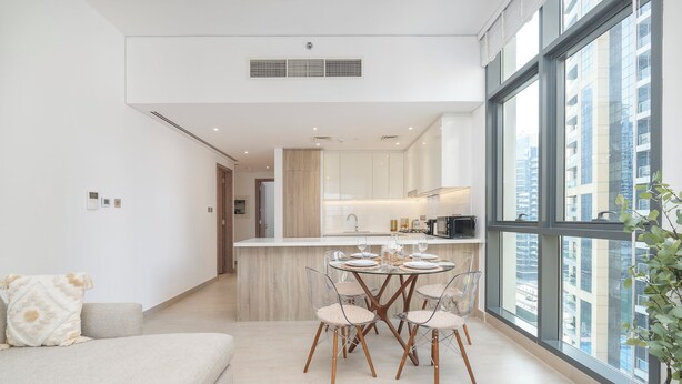 A modern apartment with a dining area, kitchen, and large windows offering city views. - Czechin - LIV Residence (Dubai)