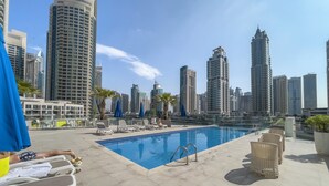 A rooftop pool with lounge chairs and umbrellas, surrounded by high-rise buildings. - Czechin - LIV Residence (Dubai)