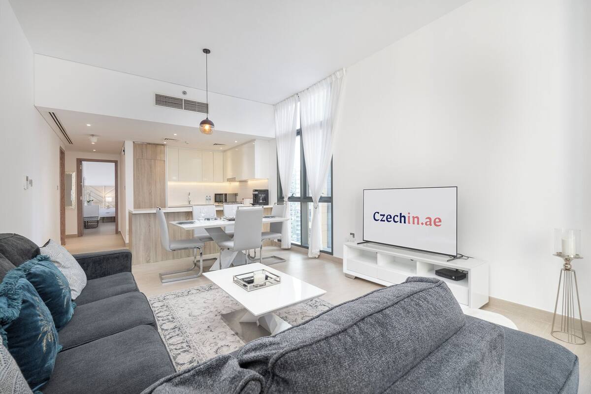 A modern living room with a grey sofa, a white coffee table, and a TV displaying 'Czechia.ae'.