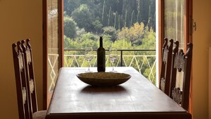 Una mesa de comedor con un tazón y copas de vino, con vista a un jardín exuberante con árboles altos.