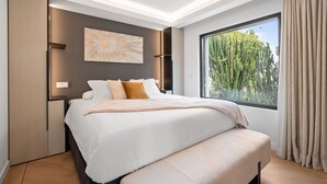 Een moderne slaapkamer met een groot bed, uitzicht op een cactustuin en een plafondlamp.