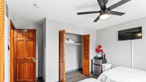 Une chambre d’hôtel équipée d’un lit, d’une armoire, d’un ventilateur de plafond, d’une télévision et d’une petite kitchenette.