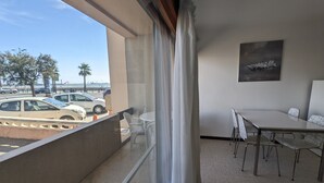 Ein Balkon mit Tisch und Stühlen, Blick auf geparkte Autos und Palmen, sowie ein Bild an der Wand.