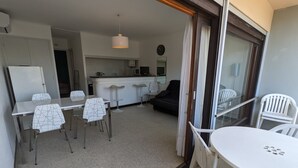 A compact living space with a dining area, kitchen, and a balcony with white plastic chairs. - Seafront T2 with AC and parking (Port-la-Nouvelle)