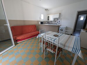 A compact living space with a kitchenette, a sofa, a dining table, and a patterned floor.