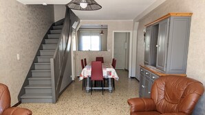 A spacious living area with a dining table set for four, a staircase, leather armchairs, and a cabinet. - Charming 2-Bedroom Villa with AC, 400m from Beach, Sleeps 5/6 (Port-la-Nouvelle)