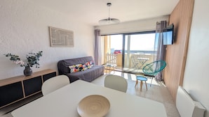 Een moderne woonkamer met een bank, een eettafel met een schaal, een balkon met stoelen en uitzicht op zee.