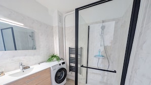 Een moderne badkamer met een douchecabine van glas, een ingebouwde wasmachine en een wastafel met spiegel.