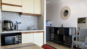 Eine kompakte Küche mit integriertem Backofen, Kaffeemaschine und Spüle. Es gibt einen Essbereich mit Tisch und Stühlen.