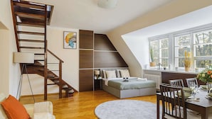 Een slaapkamer met een houten trap, een bed, een eettafel met stoelen en uitzicht op het buitengebied door grote ramen.