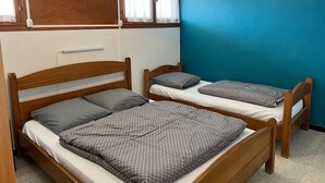 Une chambre avec deux lits en bois, chacun muni d’un oreiller et d’une couverture à carreaux.