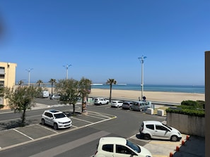 Ein Parkplatz mit mehreren Autos, ein Strand im Hintergrund und einem klaren, blauen Himmel.