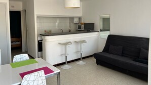 Un espace de vie compact comprenant un coin cuisine, un coin repas avec une table et des chaises, et un canapé noir.