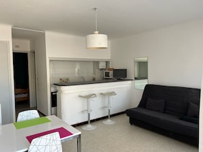 Ein kompakter Wohnbereich mit Küchenzeile, einem Essbereich mit Tisch und Stühlen sowie einem schwarzen Sofa.