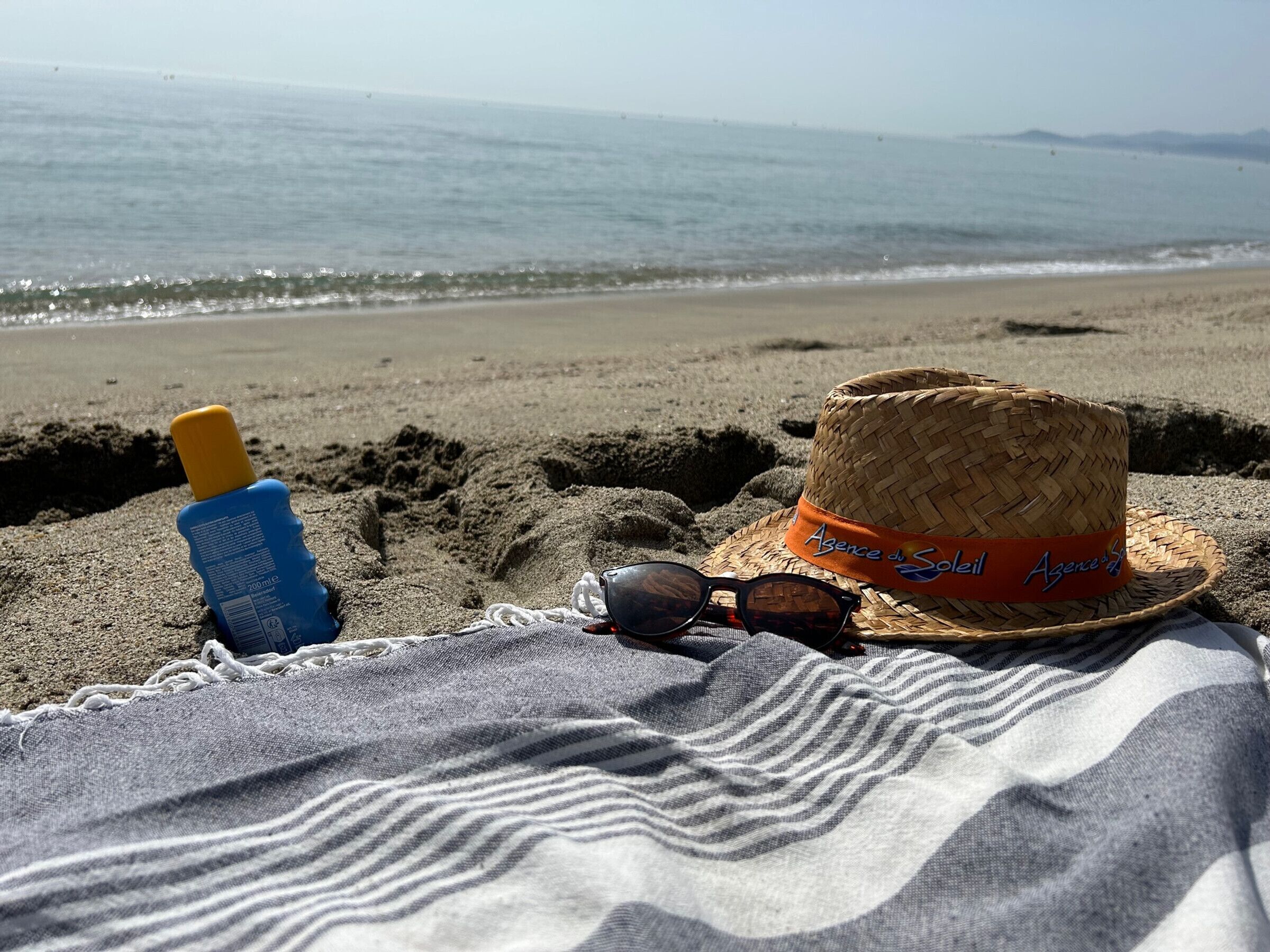 A beach scene with a straw hat, sunglasses, and sunscreen bottle on the sand.
