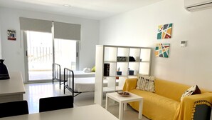Un soggiorno moderno con un divano giallo, un tavolino da caffè bianco e un mobile TV bianco. C'è una porta scorrevole in vetro che dà su uno spazio esterno.