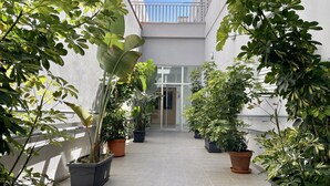 Un cortile stretto e piastrellato con vasi di piante ai lati, che conduce a un ingresso con porta in vetro.