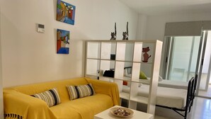 A living room with a yellow sofa, a white coffee table, and a white shelving unit with decorative items. - Beachfront apartment with air conditioning and Wi-Fi in Torrox-Costa (Torrox Costa)