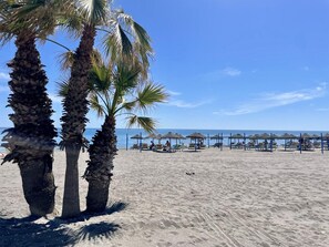 A beach with palm trees and beach umbrellas.