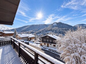 A snow-covered mountain landscape with wooden buildings, a clear sky, and a bright sun.