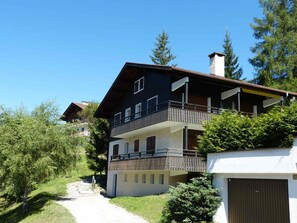 Ein mehrstöckiges Gebäude mit Balkon, umgeben von Grünpflanzen und Bäumen.