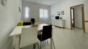 Une pièce moderne et bien éclairée, avec une table à manger, des chaises, un téléviseur posé sur un meuble et une porte donnant sur une autre pièce.