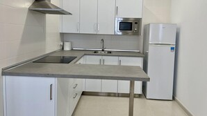 Une cuisine de taille réduite avec des meubles blancs, une hotte de cuisinière en acier inoxydable, un four à micro-ondes et un réfrigérateur.