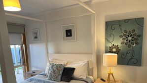 A neatly arranged bedroom with a bed, bedside table, lamp, and artwork on the wall.
