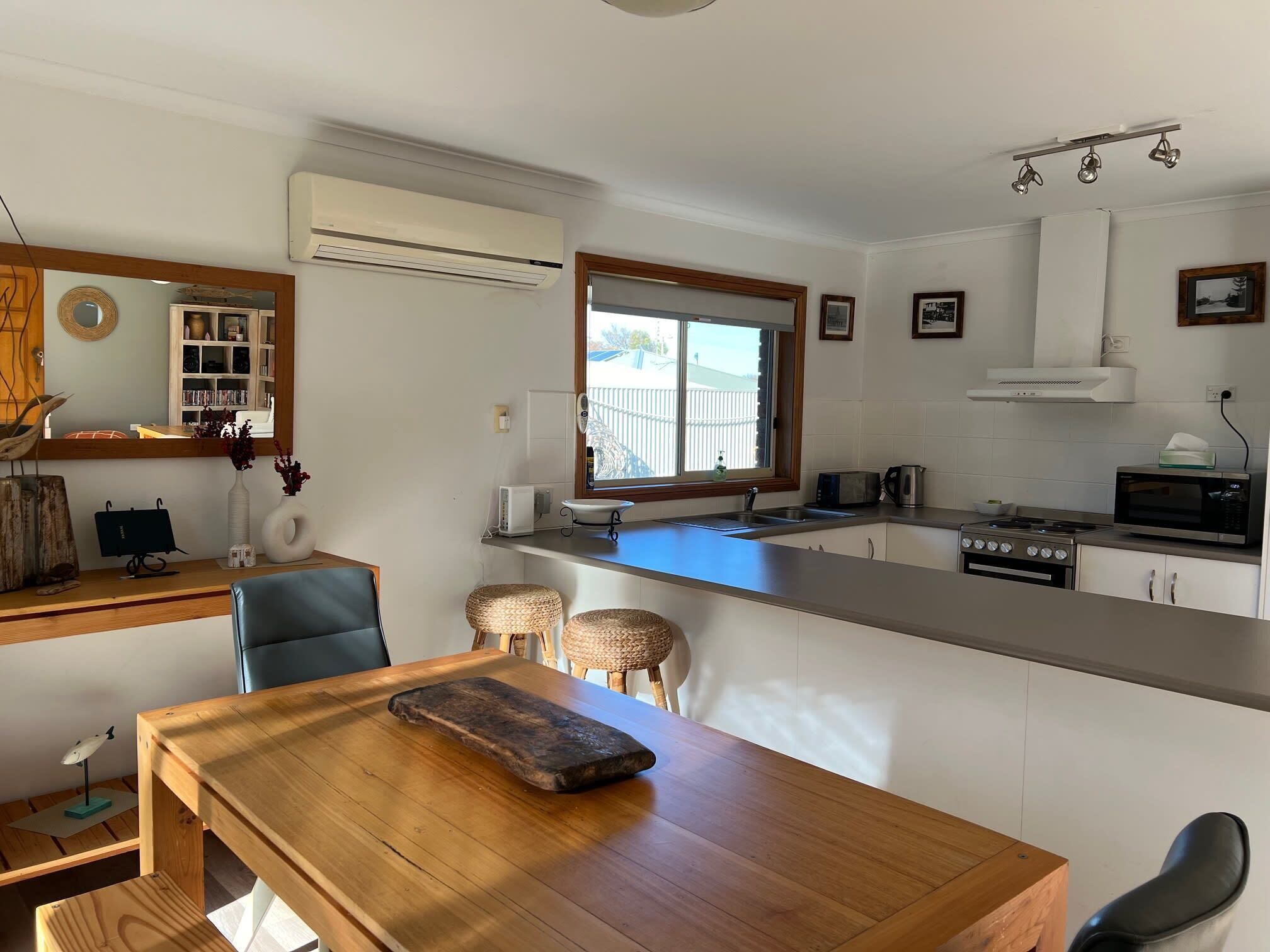 Une cuisine moderne dotée d’un îlot central, d’un coin repas avec une table en bois et d’une vue sur l’extérieur grâce à une fenêtre.