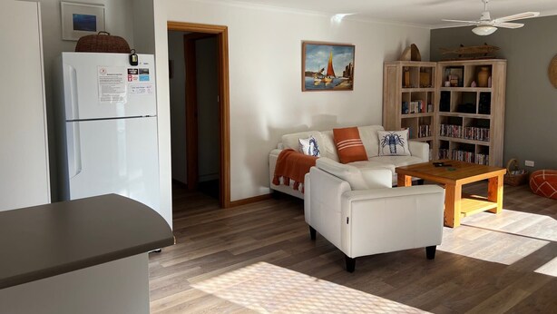 A living room with a white sofa, a wooden coffee table, a bookshelf, and a refrigerator.