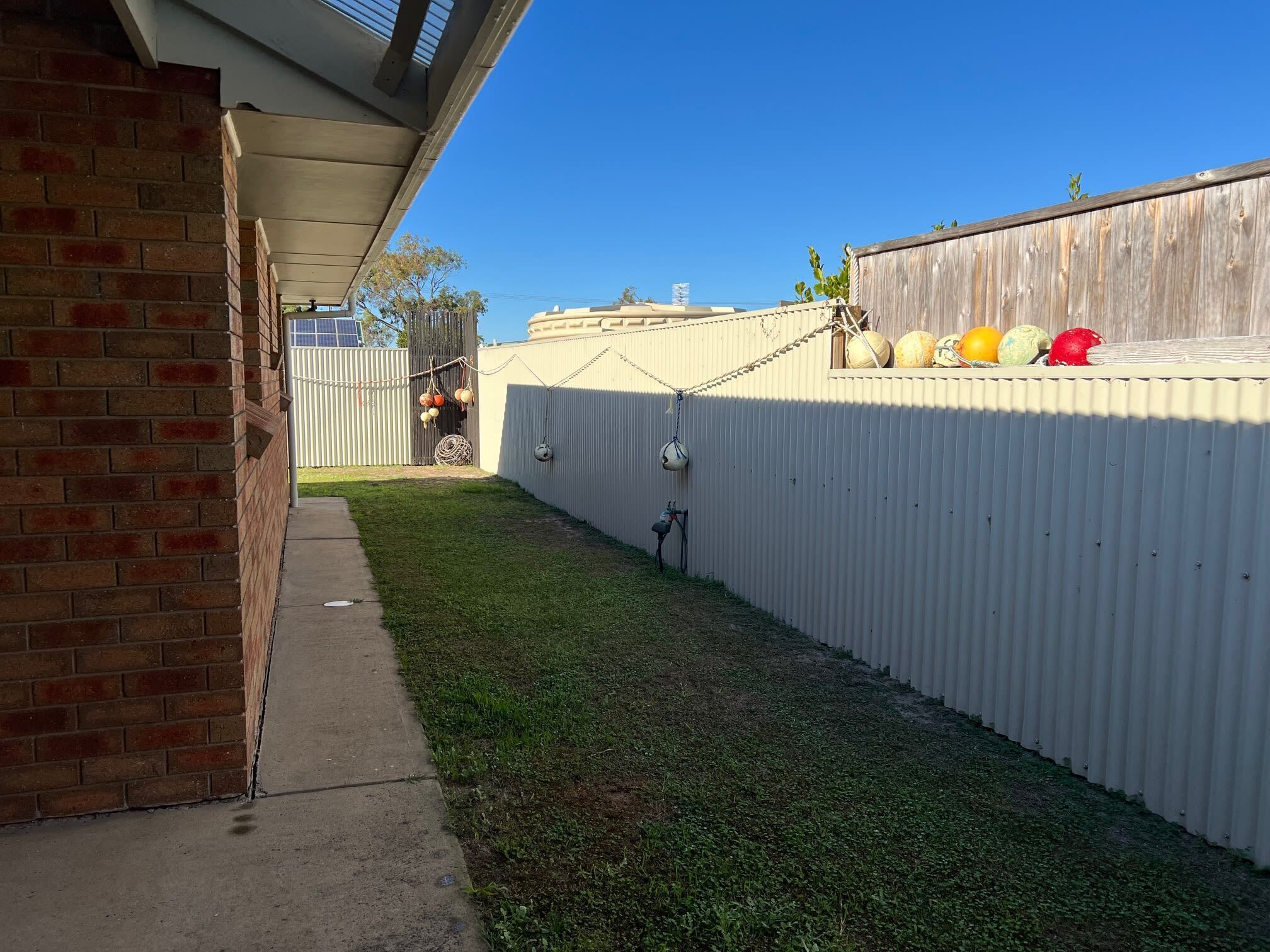 Quintal cercado com área gramada, muro de tijolos e cerca de metal corrugado.