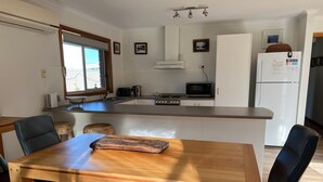 A modern kitchen with a central island, a dining table with chairs, and a refrigerator.
