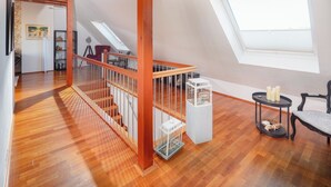 Ein geräumiger Loft mit Holzboden, einer Holztreppe, einem Oberlicht und einer gemütlichen Sitzecke mit einem kleinen Tisch und Stuhl.