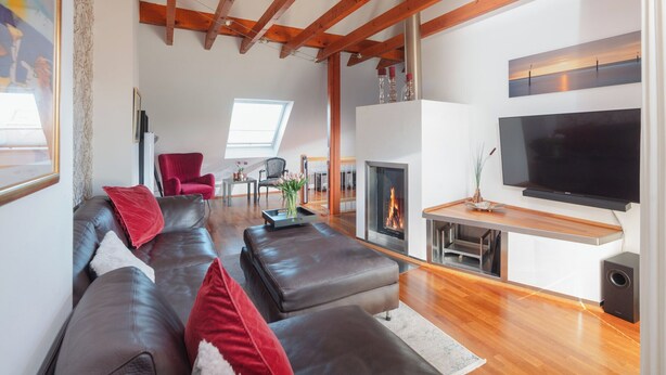 Ein modernes Wohnzimmer mit einer großen Ledersofa, einem Flachbildfernseher, einem Kamin und Holzbalken an der Decke.