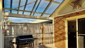 A covered patio with a grill, wooden fence, and a brick wall. - Lazy Sails Starboard  - Pets welcome outside, WiFi (Robe)