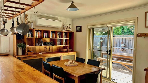 A kitchen with a wooden table and chairs, a bookshelf, and a sliding glass door leading to an outdoor patio. - Lazy Sails Starboard  - Pets welcome outside, WiFi (Robe)