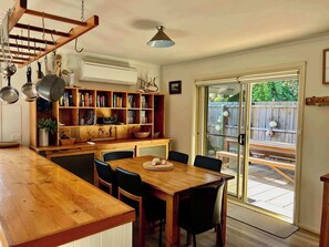 A kitchen with a wooden table and chairs, a bookshelf, and a sliding glass door leading to an outdoor patio. - Lazy Sails Starboard - Pets welcome outside, WiFi (Robe)
