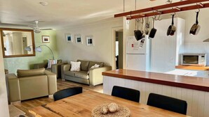 A modern kitchen with a wooden island, a dining table with chairs, a sofa, and a ceiling fan. - Lazy Sails Starboard  - Pets welcome outside, WiFi (Robe)
