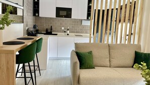 Eine moderne Küche mit weißen Schränken, einem Holztisch mit grünen Stühlen und einem beigen Sofa mit grünen Kissen.