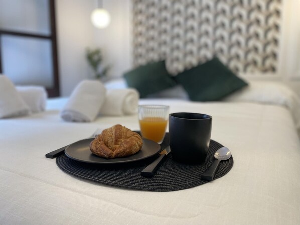 A neatly made bed with a black placemat, a croissant, a glass of orange juice, and a black mug.